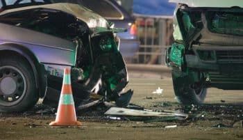 Damaged vehicles with an orange traffic cone after collision on crash site at night