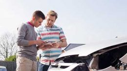 Two men standing in front of a wrecked white car exchanging insurance information