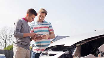 Two men standing in front of a wrecked white car exchanging insurance information
