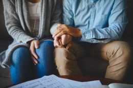 Close-up of a couple holding hands with papers on coffee table in front of them
