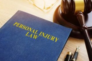 A blue personal injury law book on a desk with a pen, eyeglasses, and gavel