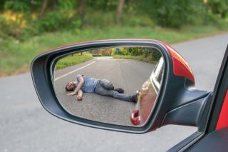 Reflection in a rearview mirror of a person lying on the road after a hit-and-run accident