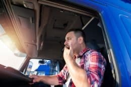 Yawning truck driver in a blue tractor-trailer cab