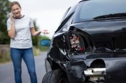 Image of a woman on the phone with a crashed black car with front end damage