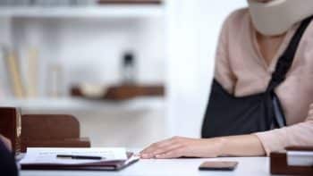 Close-up of a woman in a sling and neck brace with her hand resting on a white desk