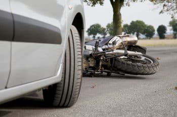 Close-up of a motorcycle overturned on the street after being hit by a silver car