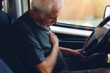Older man suffering chest pain or heart attack while driving a car