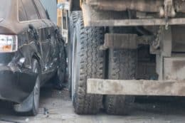 Black car wrecked in sideswipe accident with a large dump truck