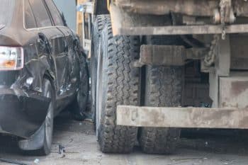Black car wrecked in sideswipe accident with a large dump truck