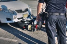 Rear view of a police officer at the scene of an accident between a white car and motorcycle.