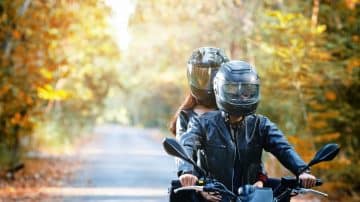 A couple riding a motorcycle with vivid fall leaves behind them