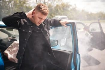 A man holding his neck getting out of a car after an accident