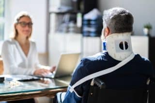 An injured man in a wheelchair speaking to a female lawyer behind a desk
